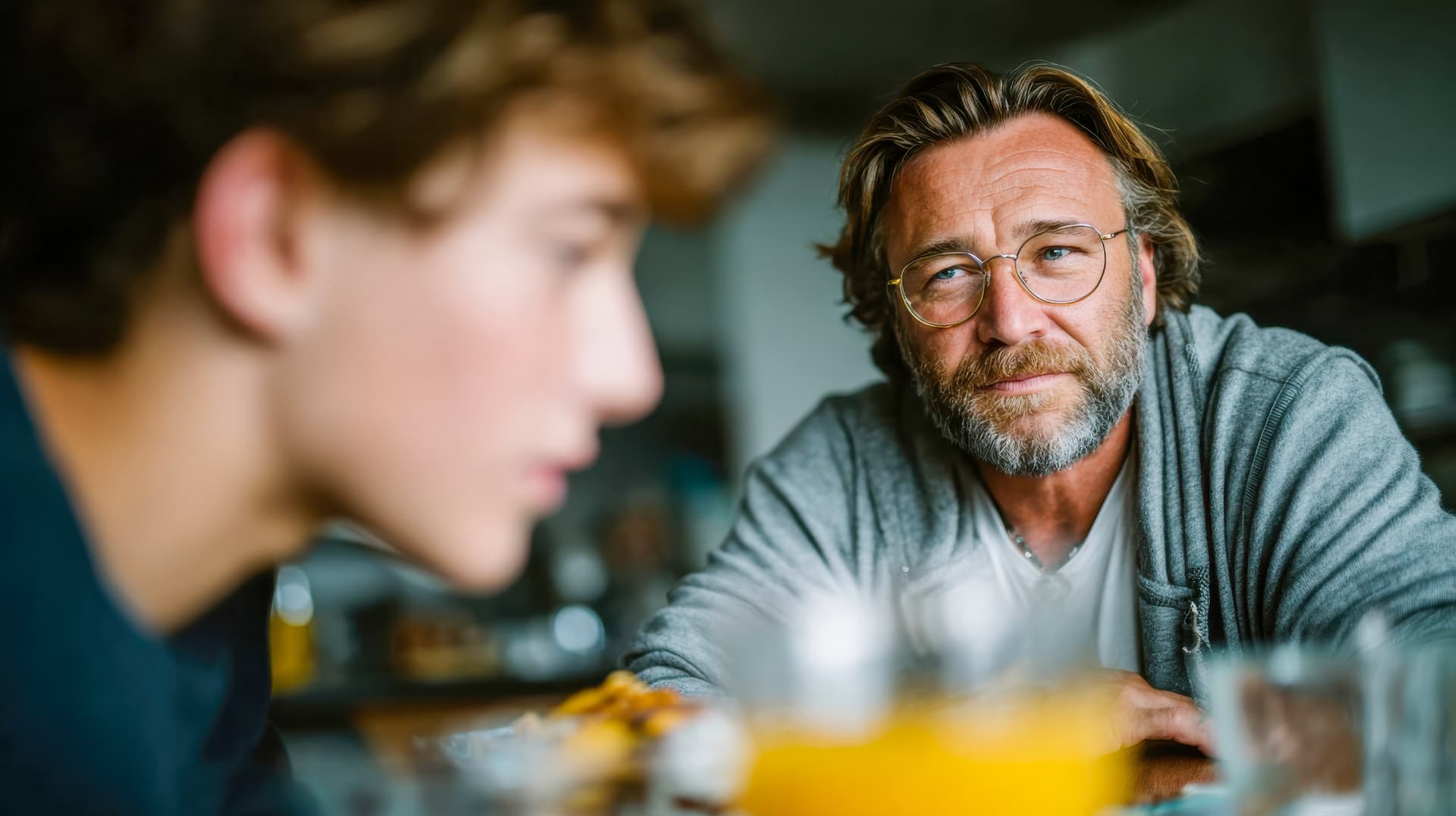 A parent and teenage son talking across the kitchen table